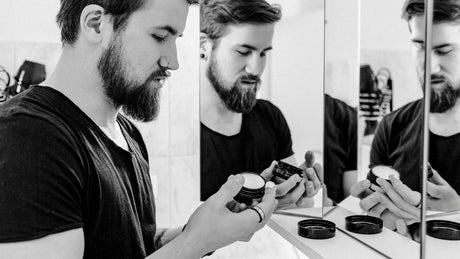Mann entnimmt Bartbalsam mit Finger aus Dose