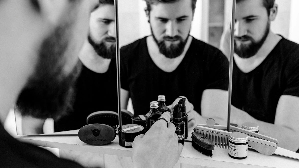 Mann greift nach Bartpflege Produkten vor Spiegel