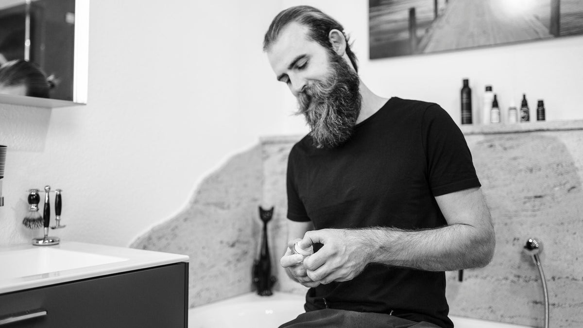 Mann nimmt Bartwichse mit Daumen aus der Dose