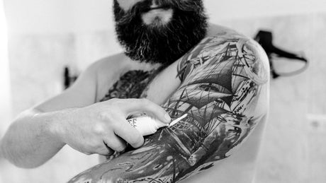 Mann cremt Tattoo Oberarm mit Tube ein