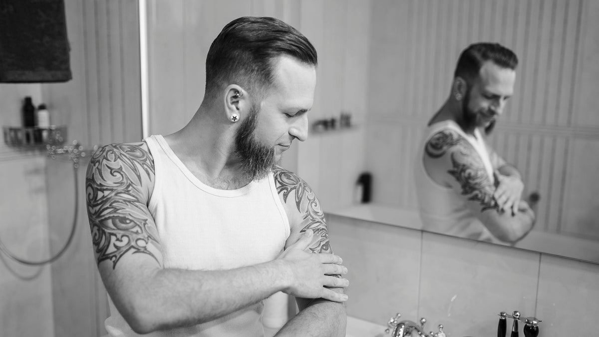 Mann cremt Tattoo Oberarm vor Spiegel ein