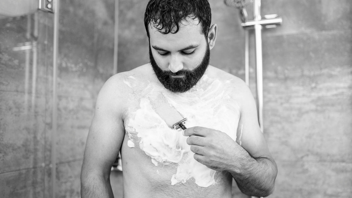 Mann rasiert Brust mit Rasierhobel unter der Dusche