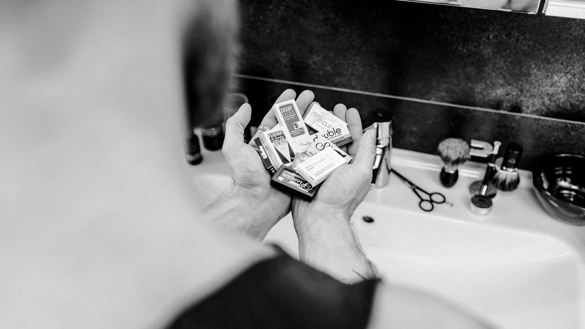 Hand hält verschiedene Rasierklingen Packungen über Waschbecken