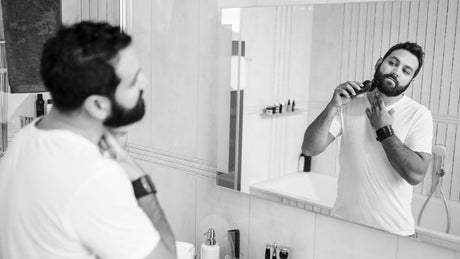 Mann trimmt Bartkontur an der Wange mit Trimmer