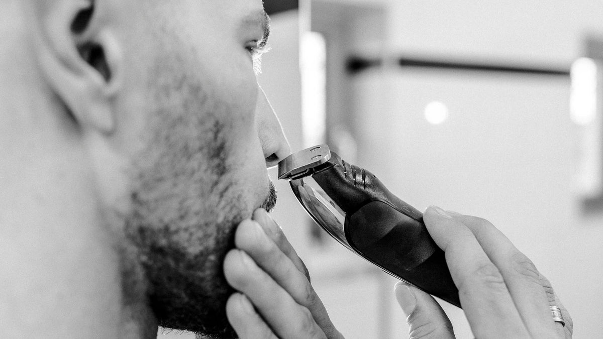 Mann trimmt Wangenkontur mit Trimmer Nahaufnahme