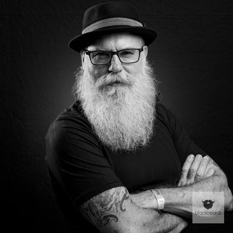 Bartträger mit Hut, Brille und grauem Vollbart, Arme verschränkt, Schwarz-Weiß-Porträt für Blackbeards